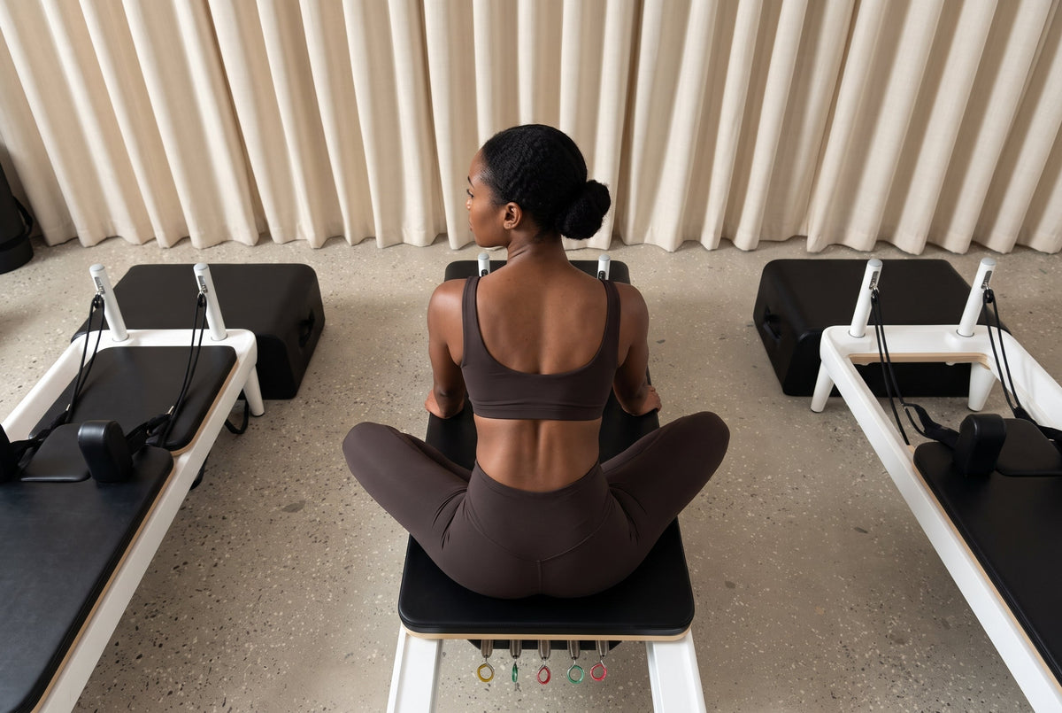 Frau sitzt aufrecht auf dem Reformer – Rücken und Haltung im Pilates Studio, Alfi Studios